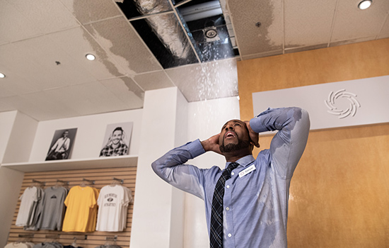 A retail business owner looks up in shock at his suddenly opened and leaking ceiling before commercial water damage restoration in Englewood, Colorado