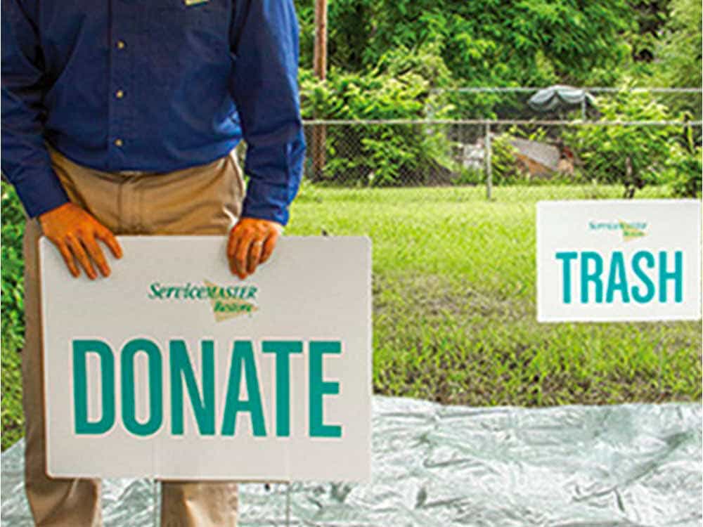 A ServiceMaster expert organizing signs labeled āDonateā and āTrashā in a yard during estate cleanout services